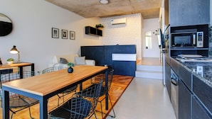 A modern kitchen with a wooden dining table, black wire chairs, and a built-in microwave. - Moderno Studio en Palermo Hollywood C3D (Buenos Aires)