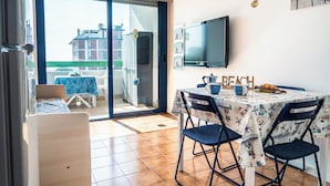 A dining area with a table set for four, a television mounted on the wall, and a view of the outside balcony. - Great Apartment With Sunny Terrace in Bibione (San Michele al Tagliamento)