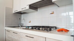 A modern kitchen with white cabinets, a stainless steel sink, and a gas stove. - Great Apartment With Sunny Terrace in Bibione (San Michele al Tagliamento)