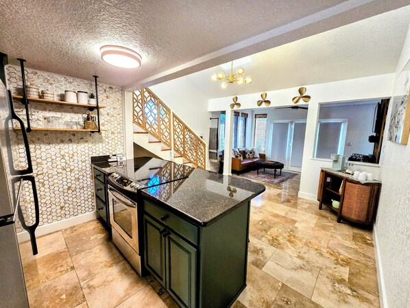 A kitchen with a central island, a staircase leading to a living area, and a dining area with a table and chairs.