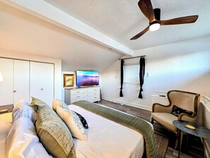 A bedroom with a bed, a TV, a ceiling fan, a dresser, and a chair.