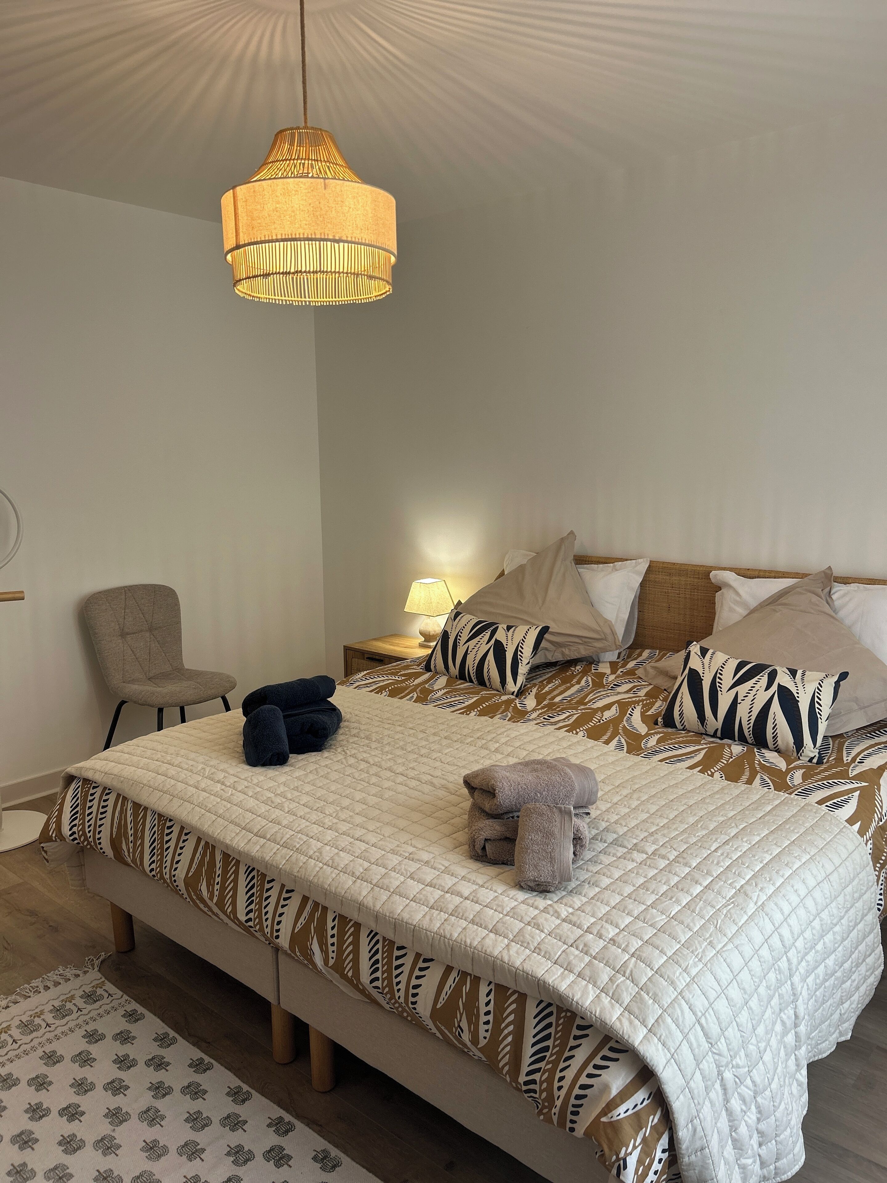 Ein ordentlich bezogenes Bett mit einem gemusterten Duvet, einer Nachttischlampe und einem Stuhl.