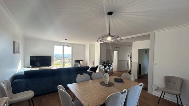 A modern living room with a dining area, a sofa, and a TV.