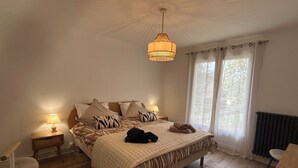 A bedroom with a bed, bedside lamps, a hanging light fixture, a window with curtains, and a radiator.