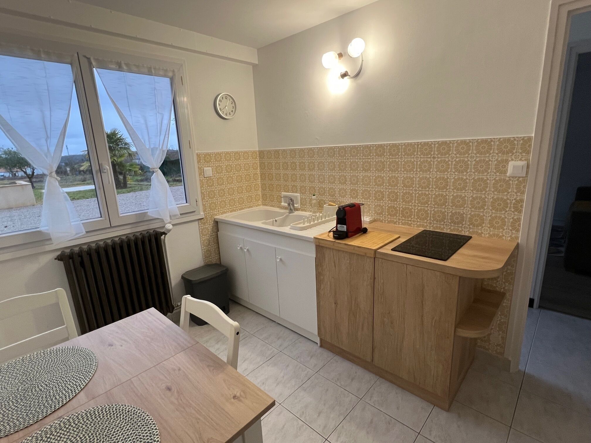 A compact kitchen with a sink, a small countertop, and a window with curtains.