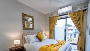Une chambre à coucher avec un lit, une table de chevet, une lampe, un miroir et une vue sur les bâtiments à l’extérieur.