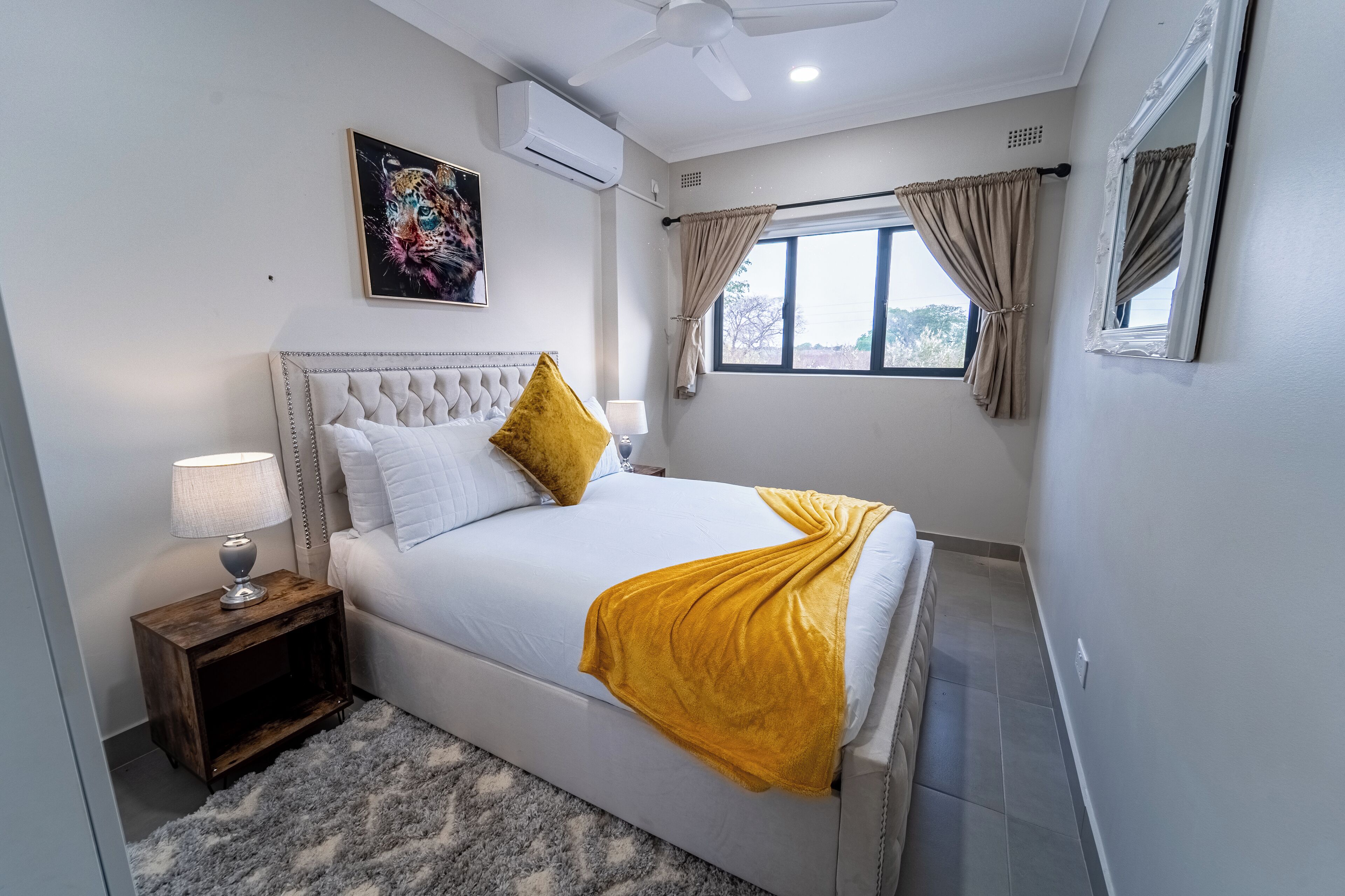 Una camera da letto con un letto, un comodino, una lampada, una ventola a soffitto e una finestra con tende.