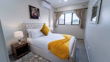 Una camera da letto con un letto, un comodino, una lampada, una ventola a soffitto e una finestra con tende.