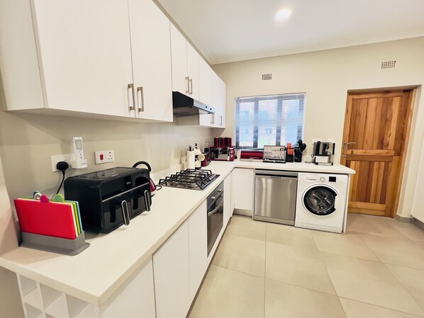 A compact kitchen with white cabinets, a gas stove, a washing machine, and a coffee maker.