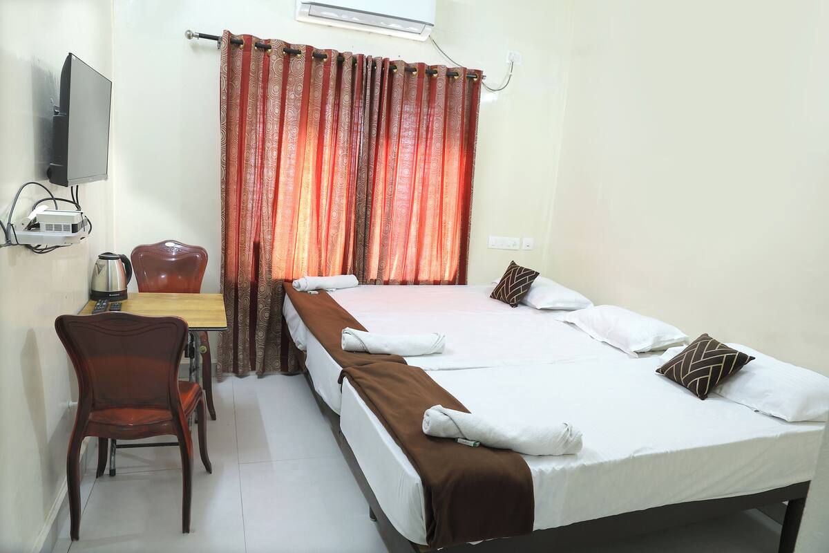 A hotel room with a bed, a desk with a kettle, a chair, and a TV.