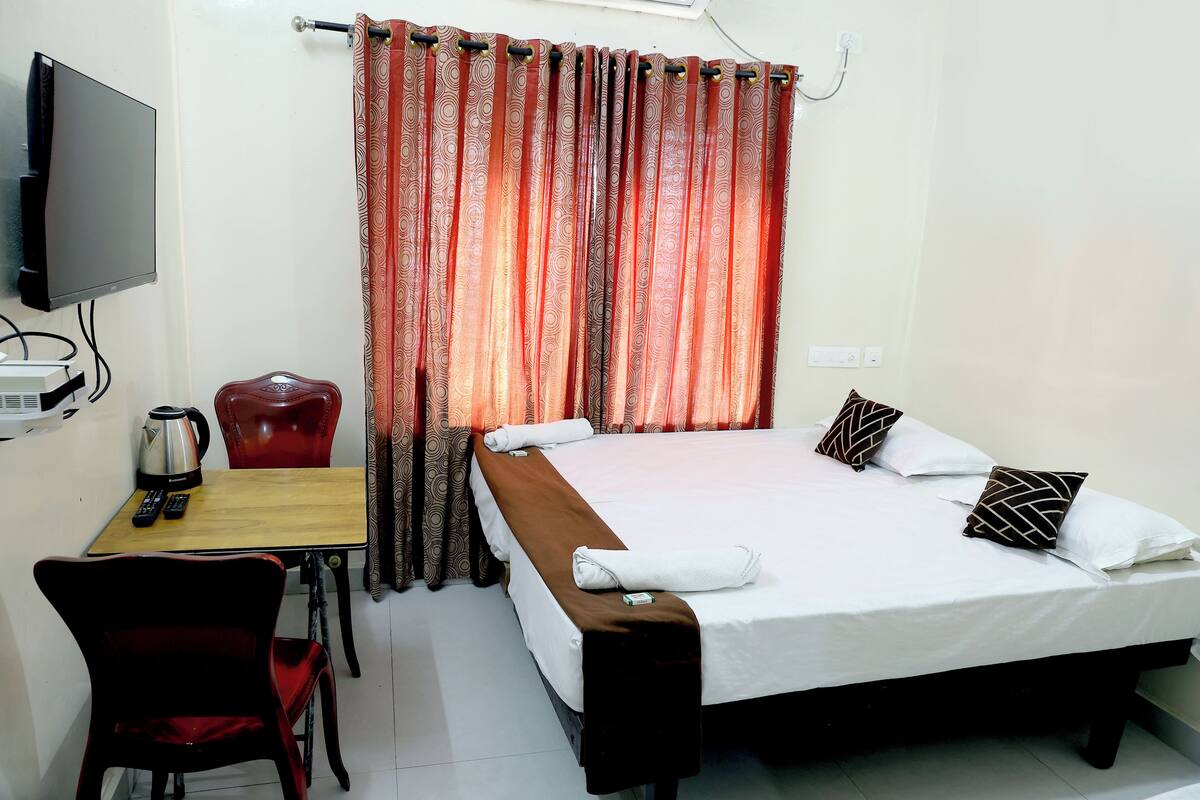 A hotel room with a bed, a desk with a chair, a television, and a curtain.