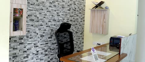A reception area with a marble counter, a black office chair, a wall with a brick pattern, a ceiling fan, and a framed artwork above the counter.