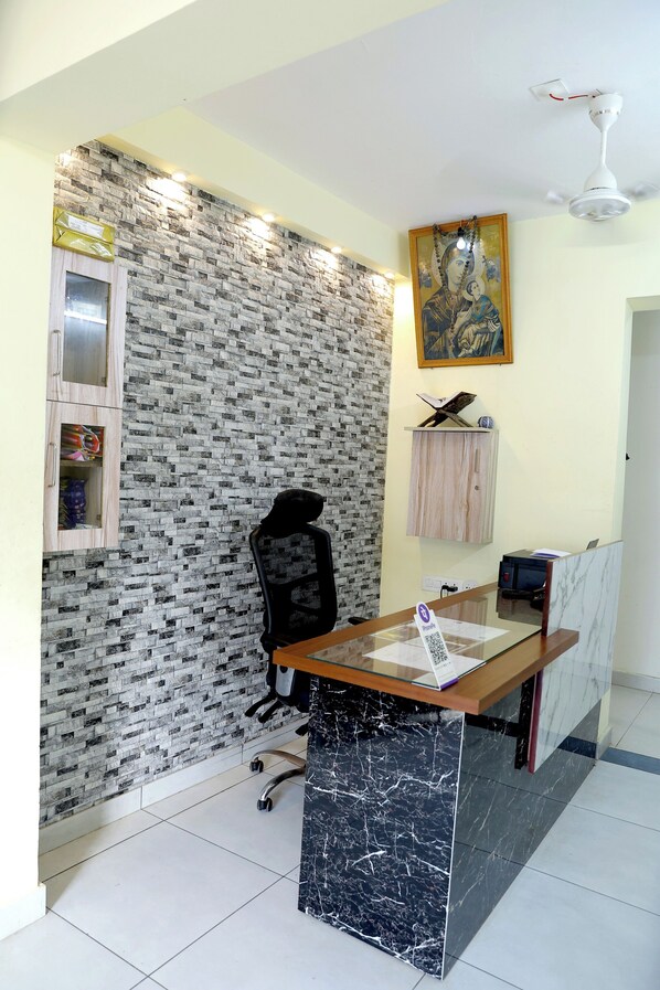 A reception area with a marble counter, a black office chair, a wall with a brick pattern, a ceiling fan, and a framed artwork above the counter. - MATHA TOURIST HOME (Thiruvananthapuram)