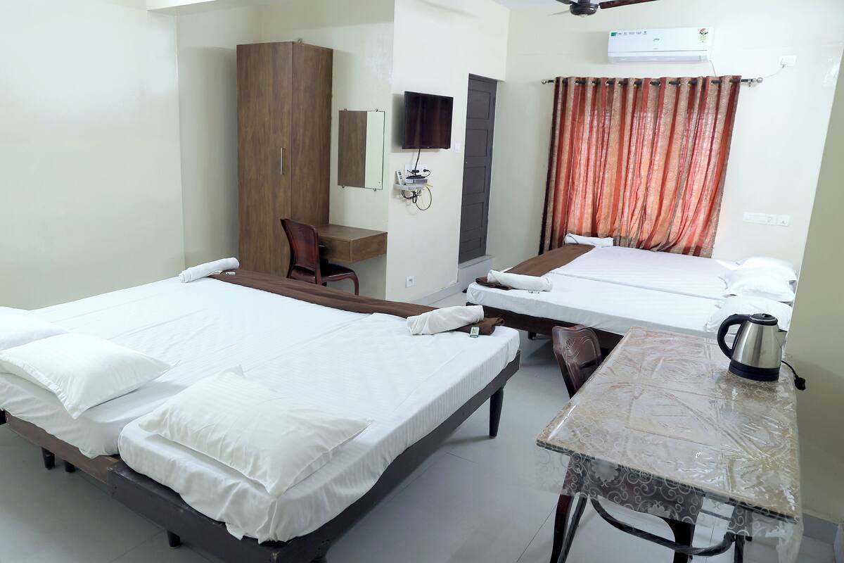 A hotel room with two beds, a desk, a chair, a TV, and an air conditioning unit.