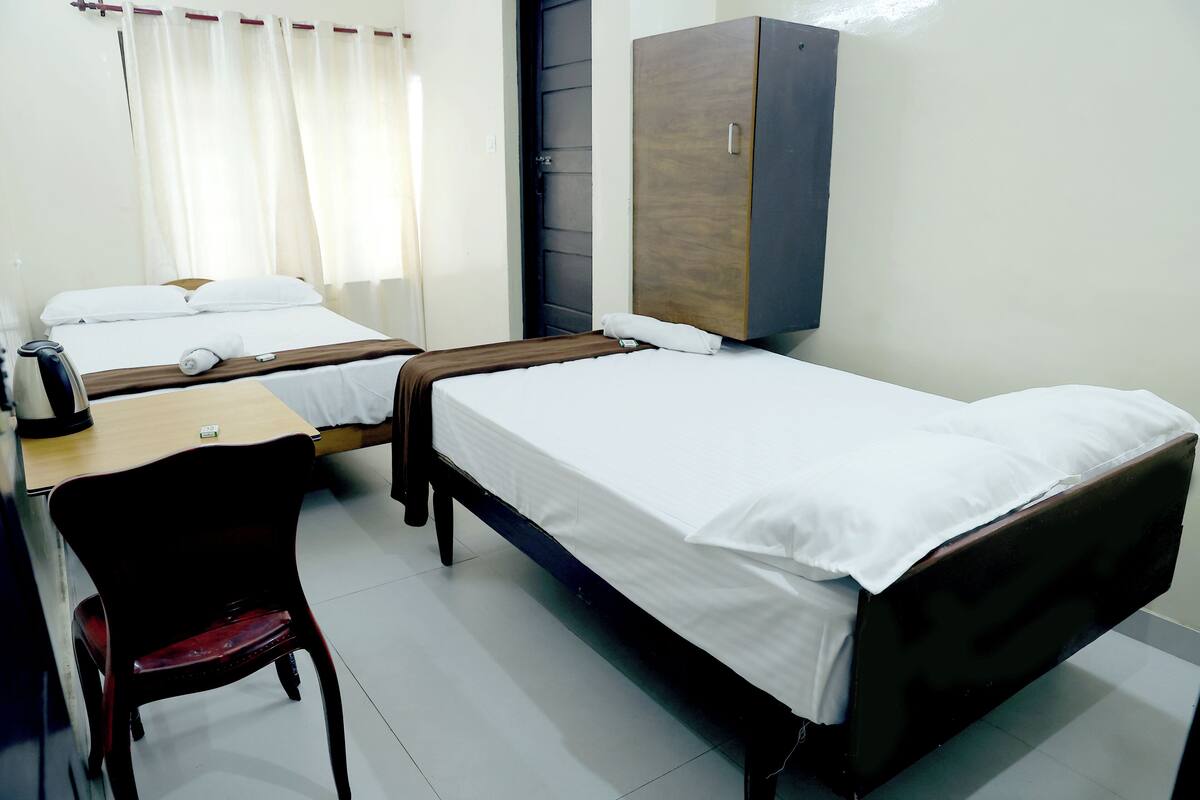 A hotel room with two single beds, a wooden wardrobe, a desk with a chair, and a window with curtains.