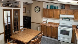 Una cocina con armarios de madera, una mesa de comedor con sillas, un reloj en la pared y un ventilador de techo.