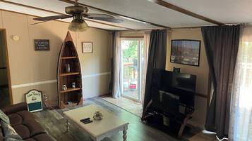 A living room with a ceiling fan, a coffee table, a sofa, a bookshelf, a TV, and a sliding glass door leading to an outdoor area.