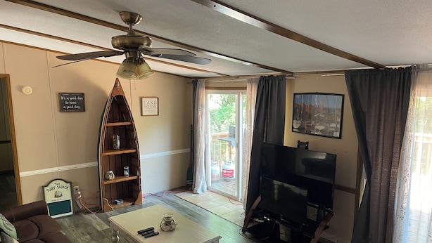 Una sala de estar con ventilador de techo, una mesa de centro, un sofá, una estantería, un televisor y una puerta corrediza de vidrio que da a un área exterior.