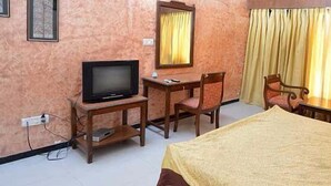A hotel room with a bed, a television on a wooden stand, a desk with a chair, and a window with curtains. - Tikkar Taal Morni Hills (Panchkula)