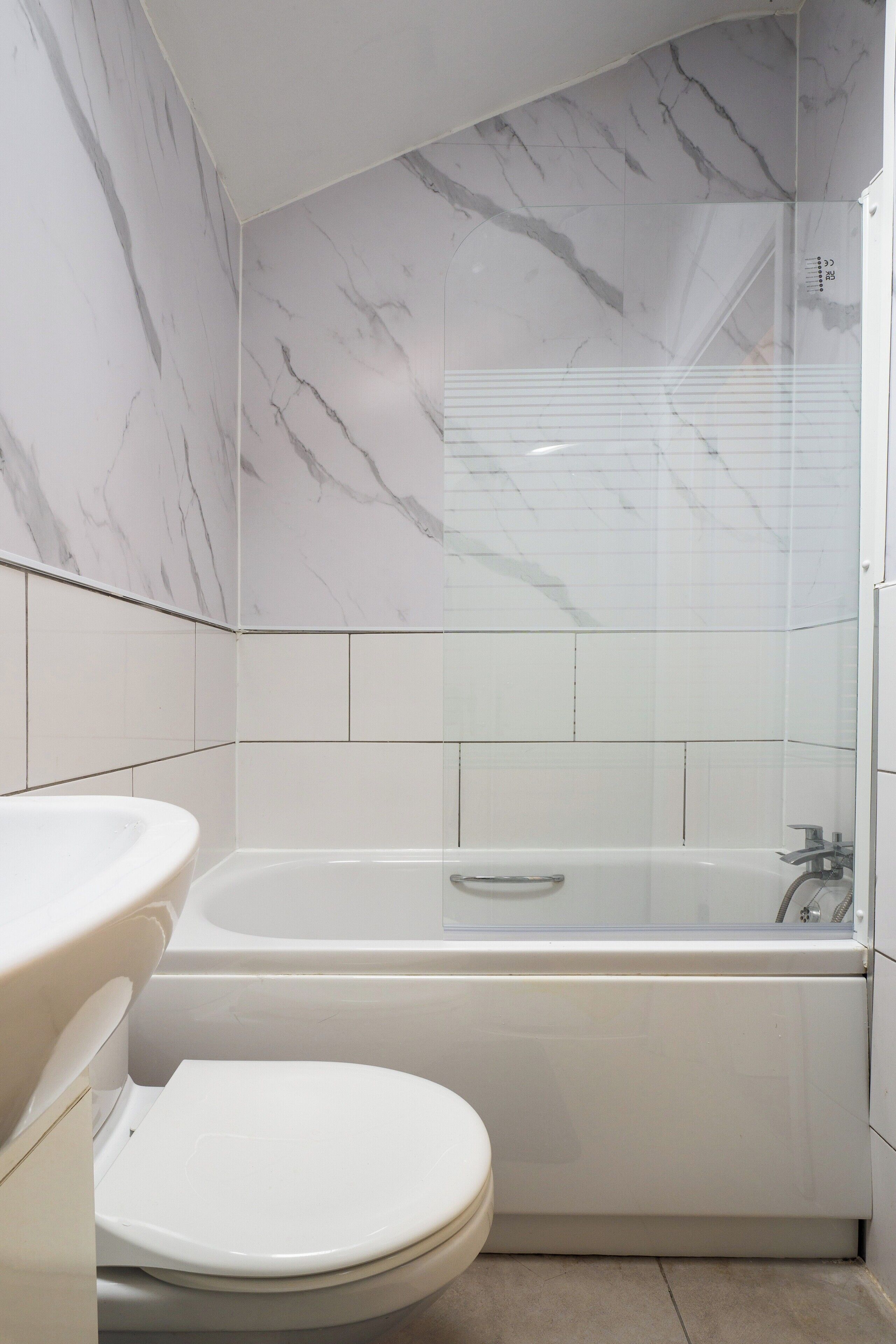 A bathroom with a marble wall, a bathtub, and a toilet.