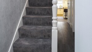 A staircase with carpeted steps and a white balustrade leading to a kitchen area. - Dartford - 3 Bed House- Sleeps7 - Garden (Dartford)