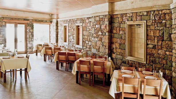 A restaurant with stone walls and wooden tables, featuring a high ceiling and large windows. - Troiada Hotel (Gokceada)