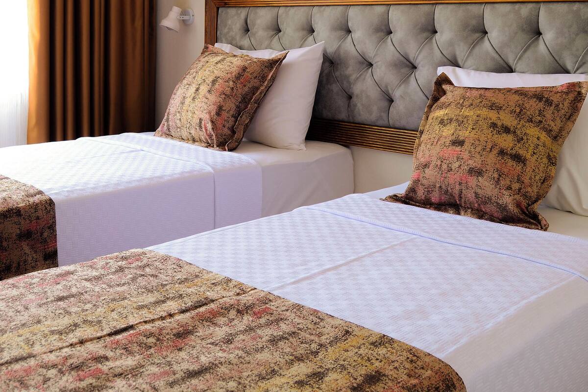 Habitación de hotel con dos camas, un cuadro grande en la pared y una ventana con cortinas.