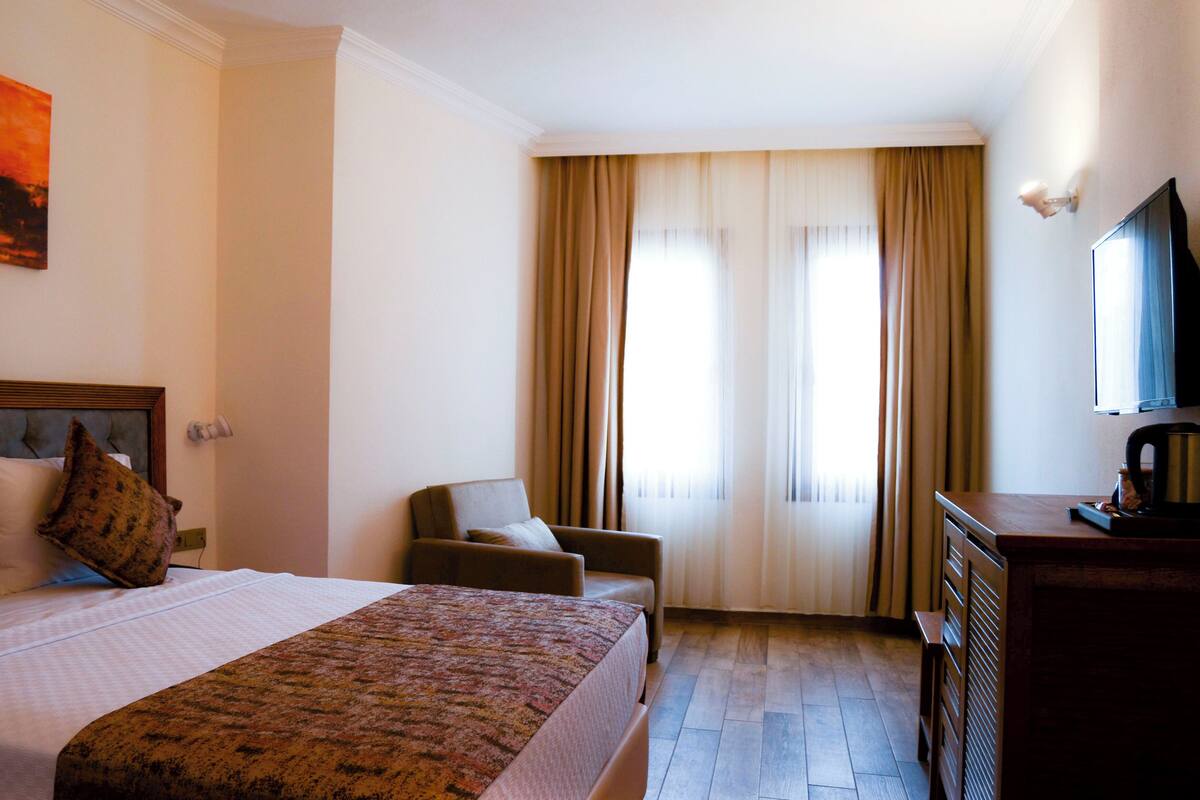 Habitación de hotel con una cama grande, un sofá, un escritorio con televisor y una ventana con cortinas.