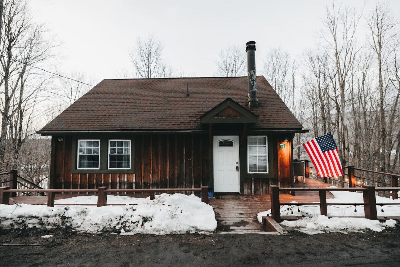 Une cabane en bois avec une porte blanche, une cheminée et un drapeau américain.