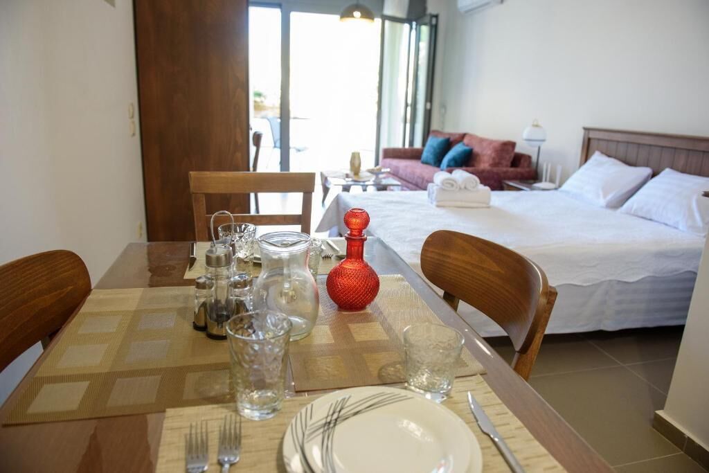A hotel room with a dining area set for two, a bed with white linens, and a view of the outdoors.
