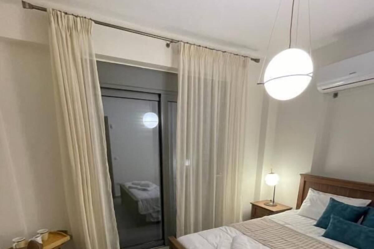 A hotel room with a bed, a desk, a chair, a nightstand, and a window with curtains.
