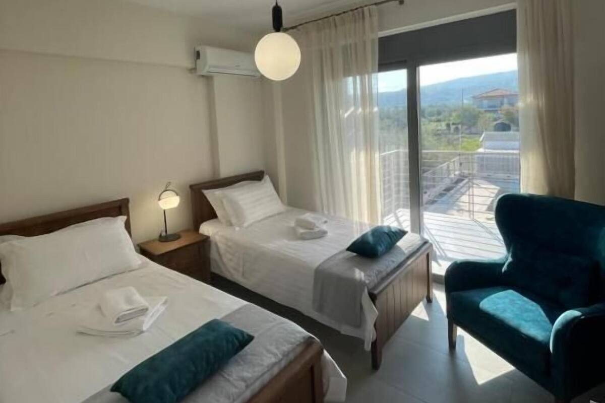 A hotel room with two beds, a blue armchair, and a balcony with a view.