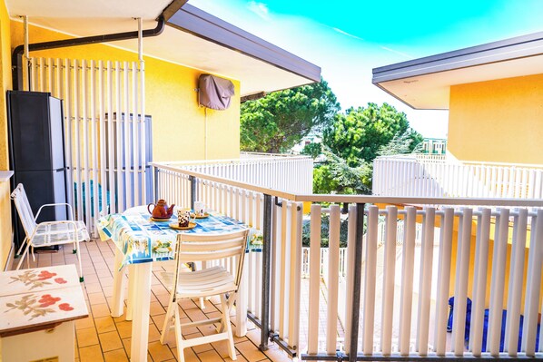 Un balcone con tavolo e sedie, un frigorifero e un parapetto bianco.