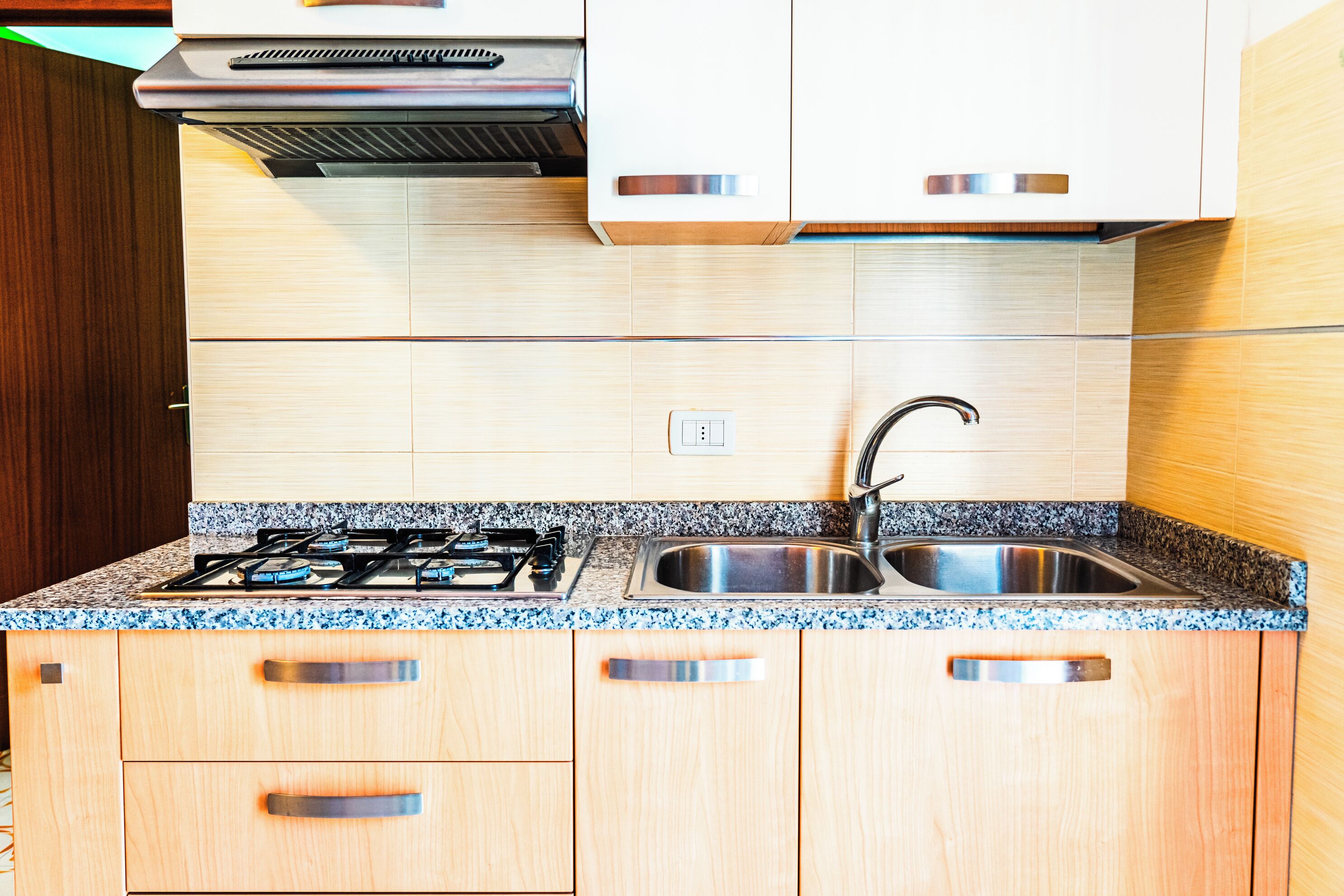 A kitchen with wooden cabinets, a granite countertop, a stainless steel sink, and a gas stove.