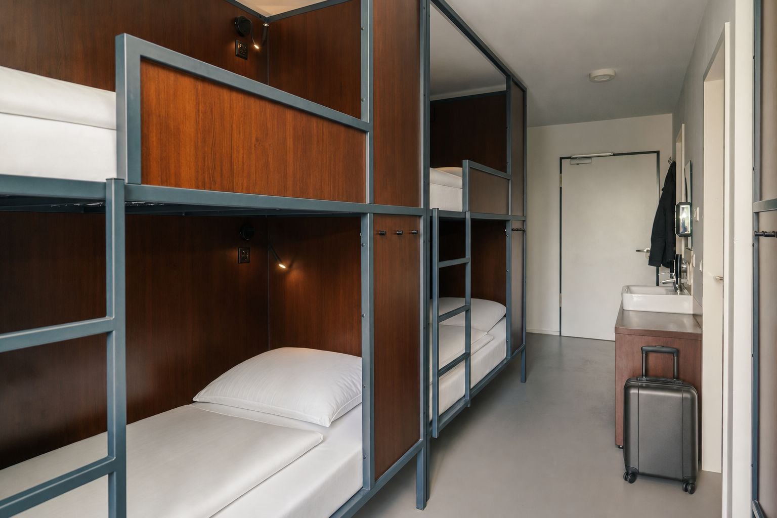 Habitación de hotel con literas, un baño pequeño y una maleta.