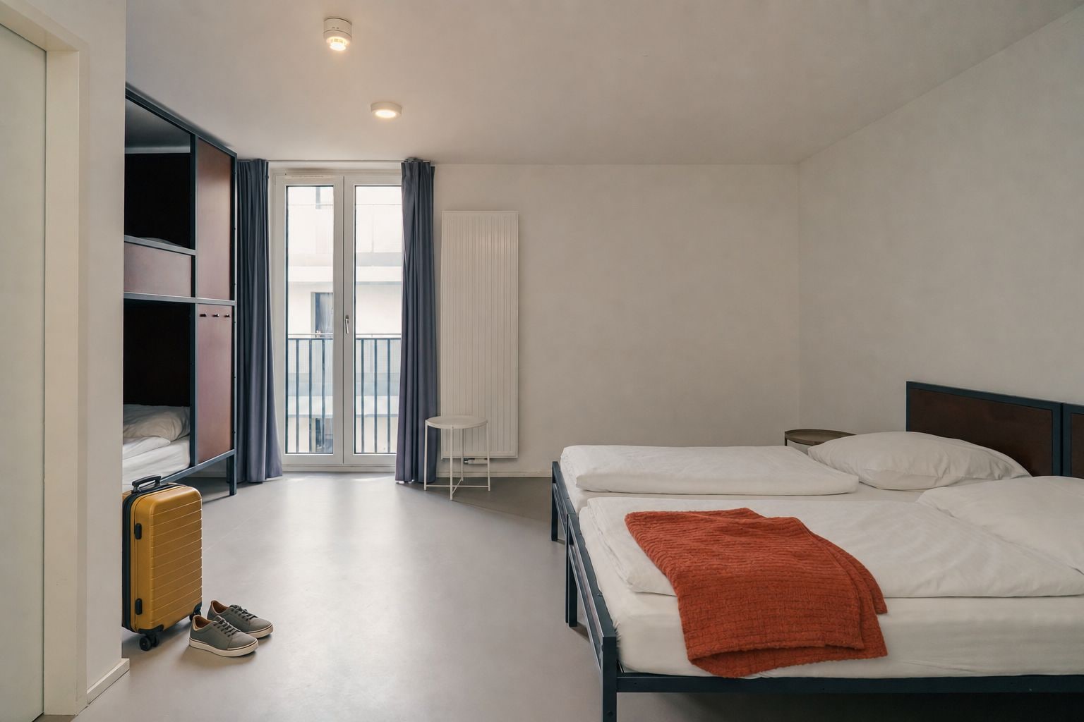 Ein Hotelzimmer mit einem Bett, einem Koffer, einem Sessel und einem Fenster mit Vorhängen.