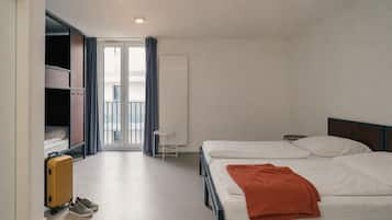 Ett hotellrum med en säng, en resväska, en stol och ett fönster med gardiner.