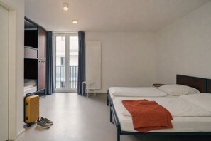 Une chambre d’hôtel avec un lit, une valise, une chaise et une fenêtre avec des rideaux.