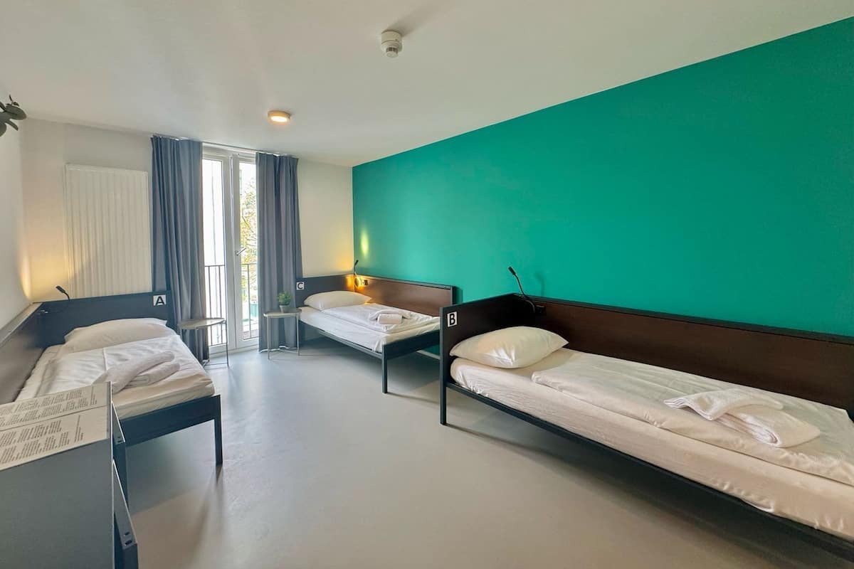 A hotel room with two single beds, a window with curtains, a small table, and a green accent wall.
