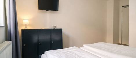 A hotel room with a bed, a wardrobe, a flat-screen TV, a lamp, and a cup on the wardrobe.