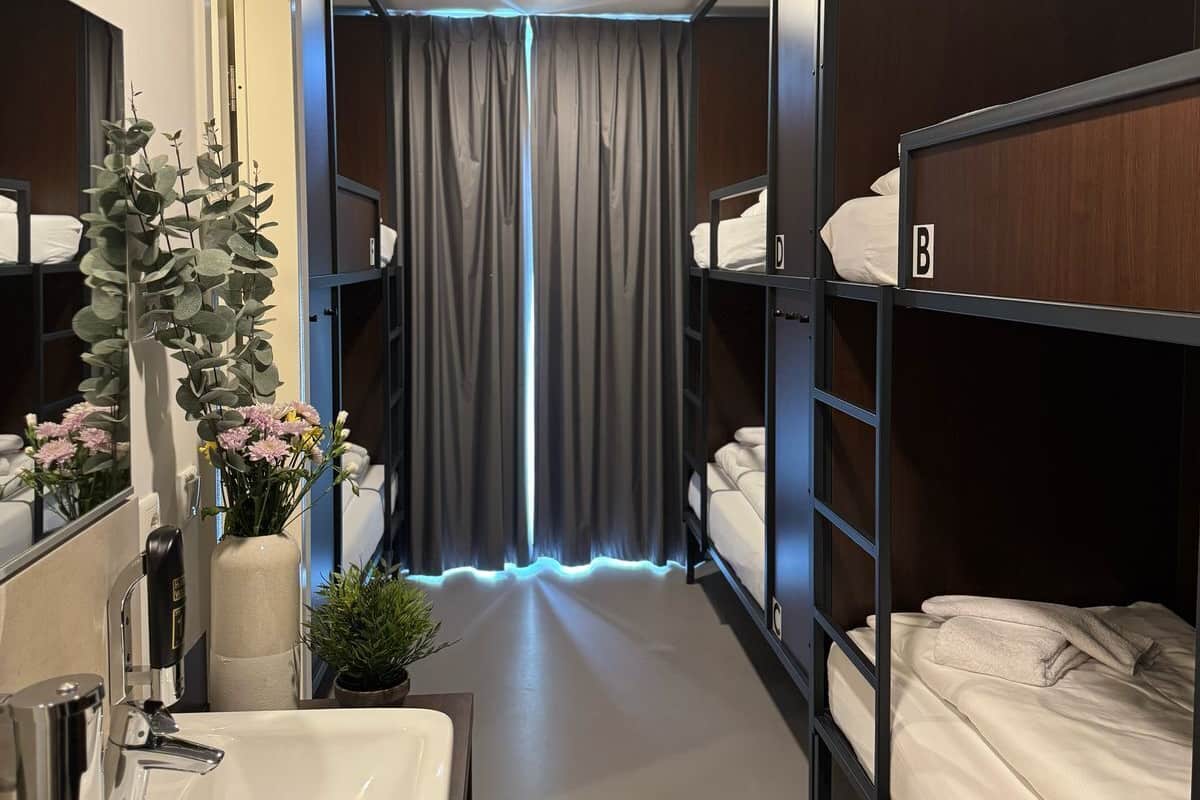 A hotel room with bunk beds, a bathroom with a sink and mirror, and a curtain with a blue light.