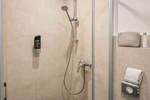 Un espace douche équipé d’un pommeau de douche à main, d’un robinet mural et d’un porte-serviettes avec une serviette pliée.