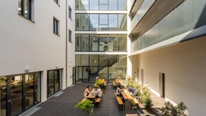 Ein modernes Gebäude mit Innenhof, Sitzgelegenheiten im Freien und einer Treppe zu einer oberen Ebene.