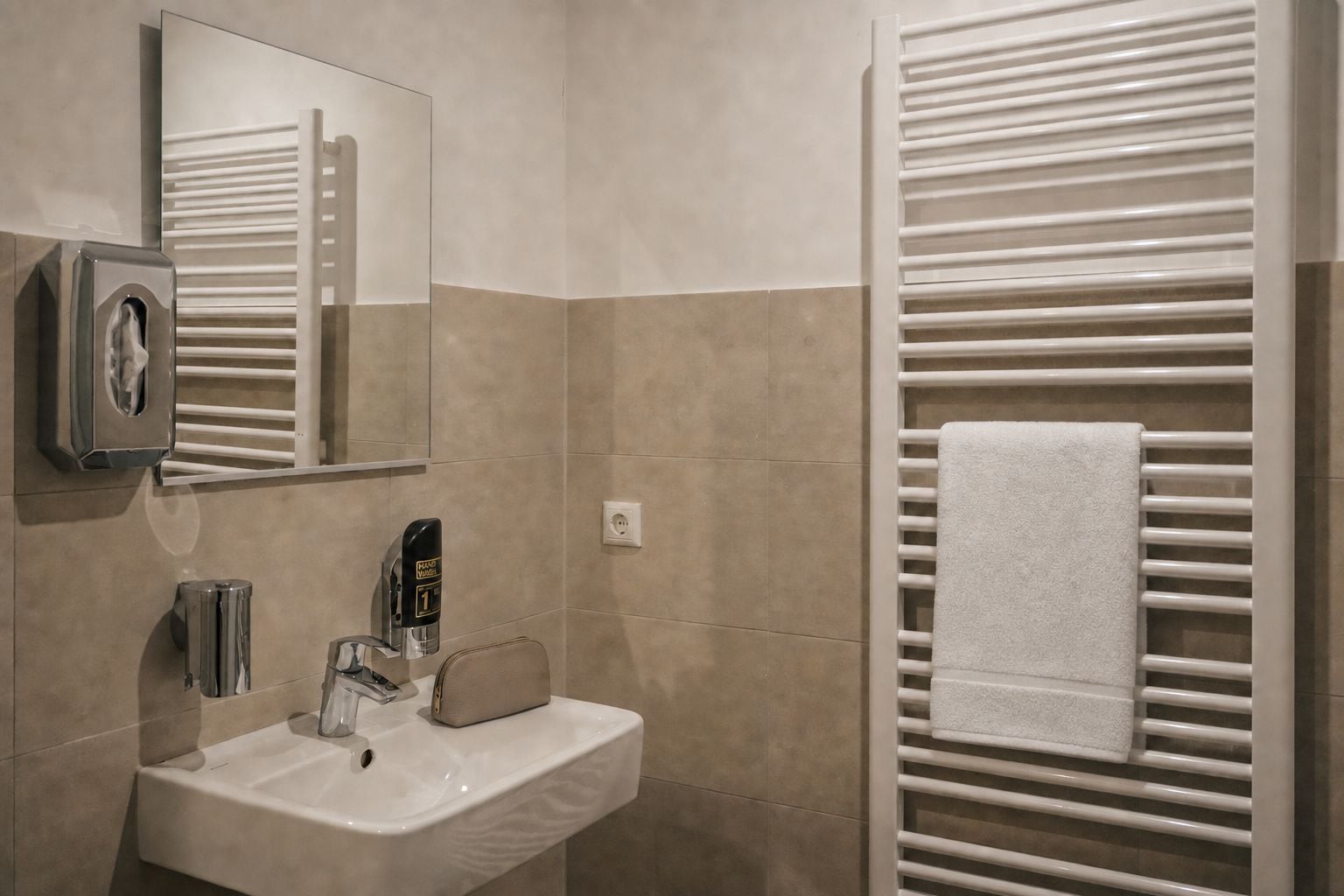 Ein Badezimmer mit Waschbecken, Spiegel, Handtuchhalter und Handdesinfenspender.