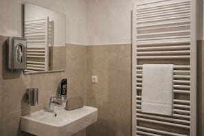 Een badkamer met een wastafel, spiegel, handdoekhouder en een handdesinfecteerder.