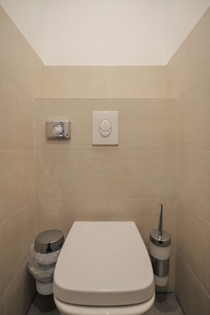 A modern bathroom with a toilet, a trash bin, and a bidet.