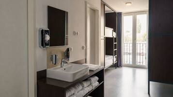 A modern bathroom with a double sink, a mirror, a towel rack, and a view of the outside through a glass door.