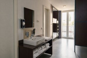 Une salle de bain moderne avec un double vasque, un miroir, un porte-serviettes et une vue sur l’extérieur grâce à une porte en verre.