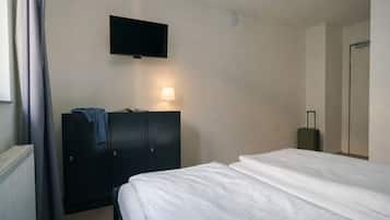Una habitación de hotel con una cama, un televisor montado en la pared, un armario y una maleta.