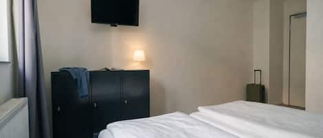 A hotel room with a bed, a TV mounted on the wall, a wardrobe, and a suitcase.
